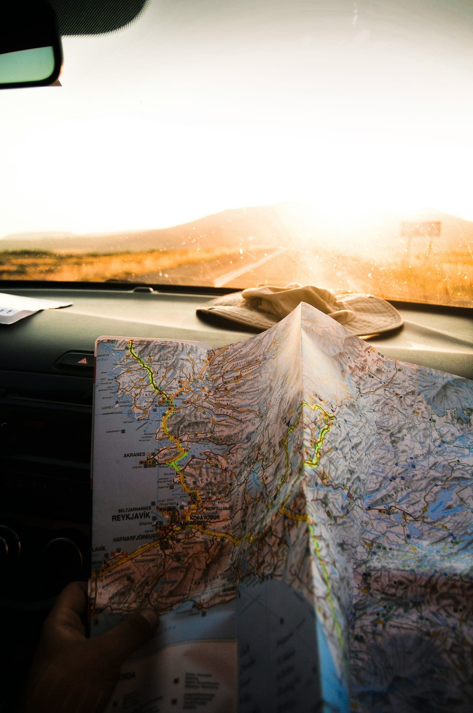 A folded road map held up against a car dashboard as the sun sets ahead